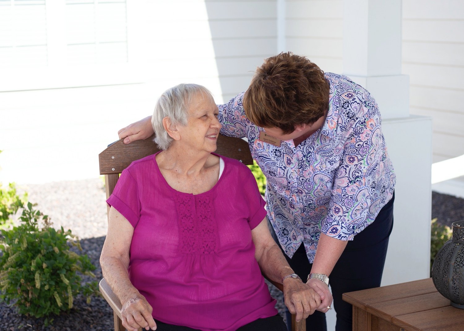 A staff member standing next to a senior resident on the patio