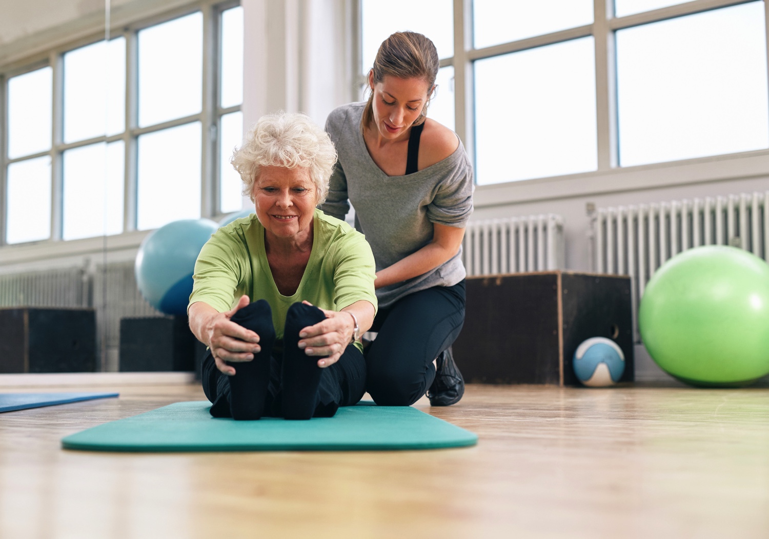 Elderly woman being helped by her instructor in the gym