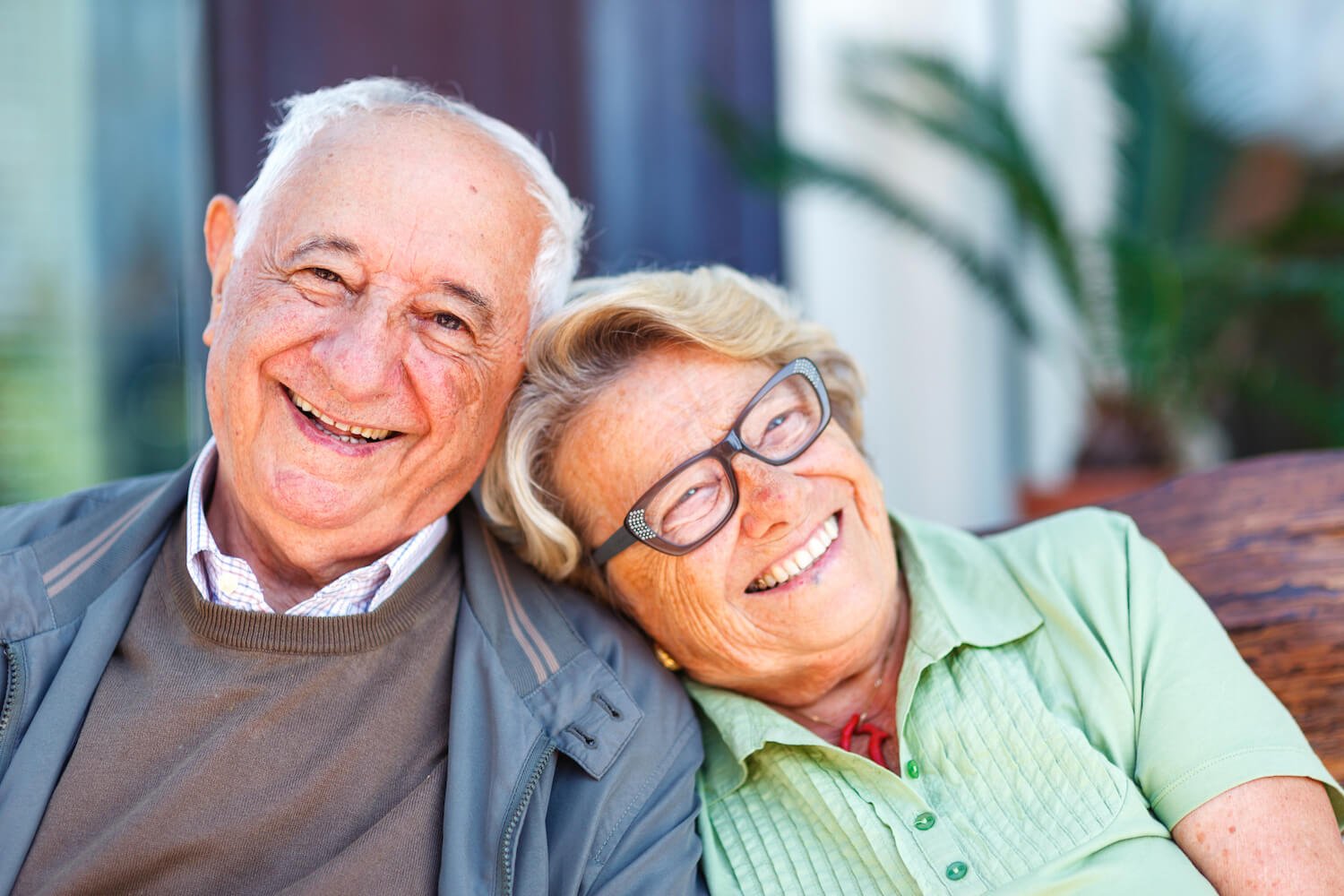 A happy senior couple, the woman leaning her head on the man's shoulder as they smile at the camera