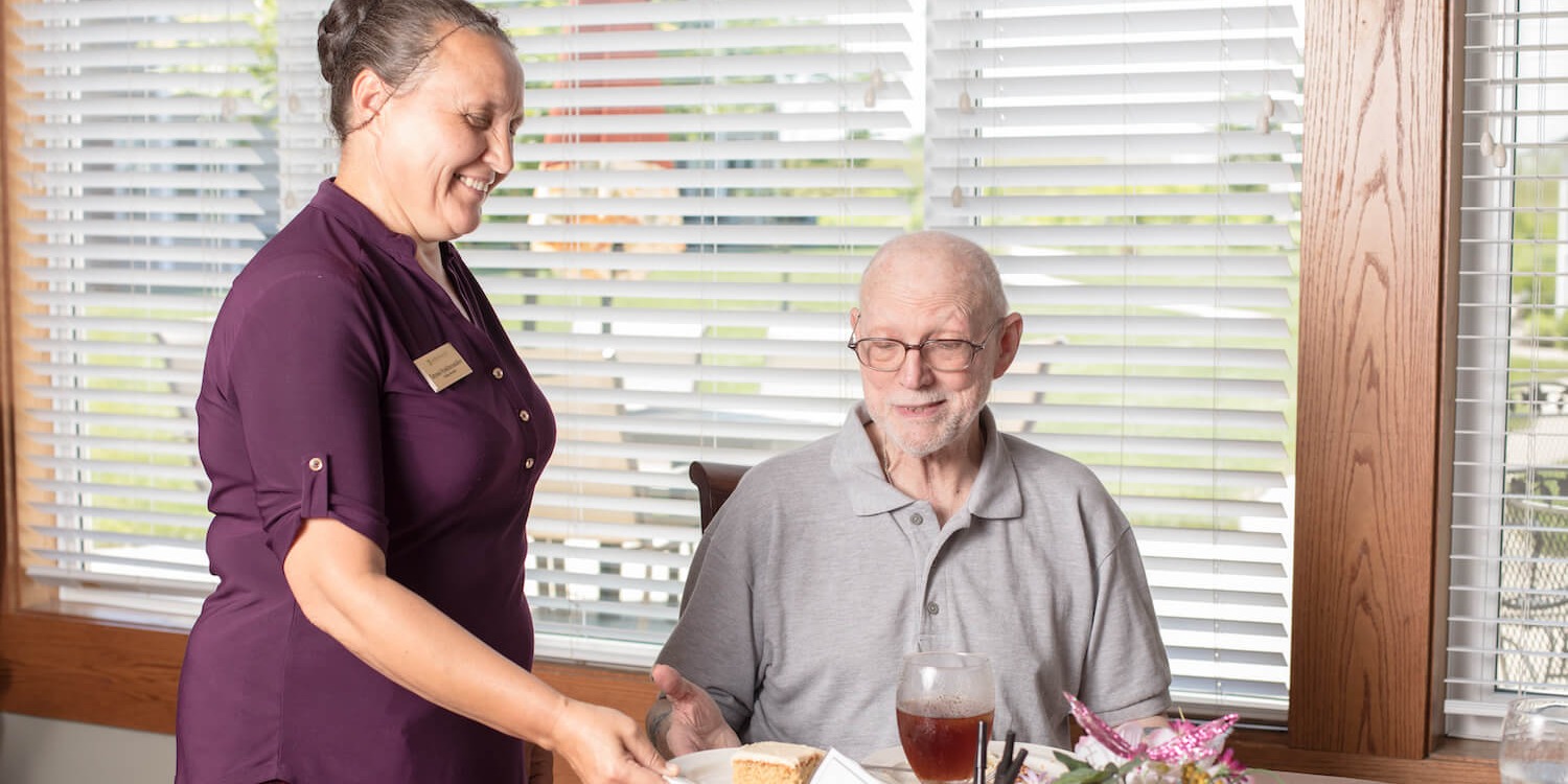 Senior living employee serving food to senior man