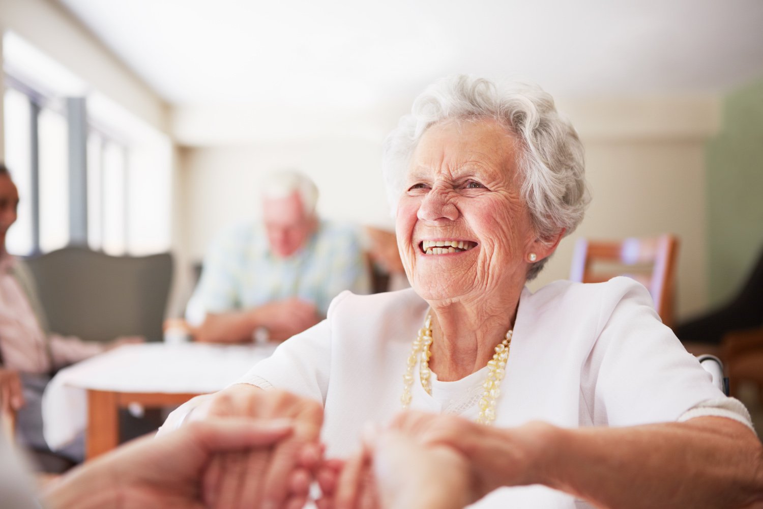 A senior woman smiling and holding the hands of someone out of frame