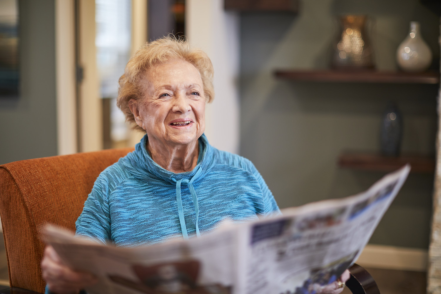 Resident reading a newspaper in a living room chair