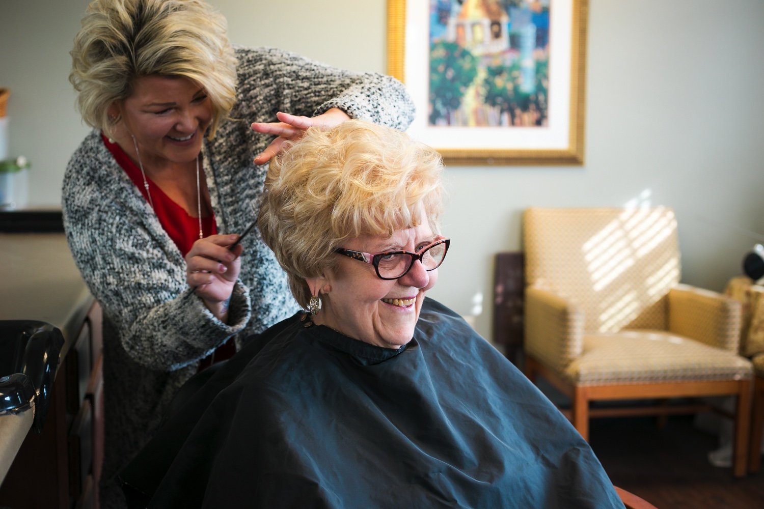 Senior community resident woman smiling while receiving a haircut.