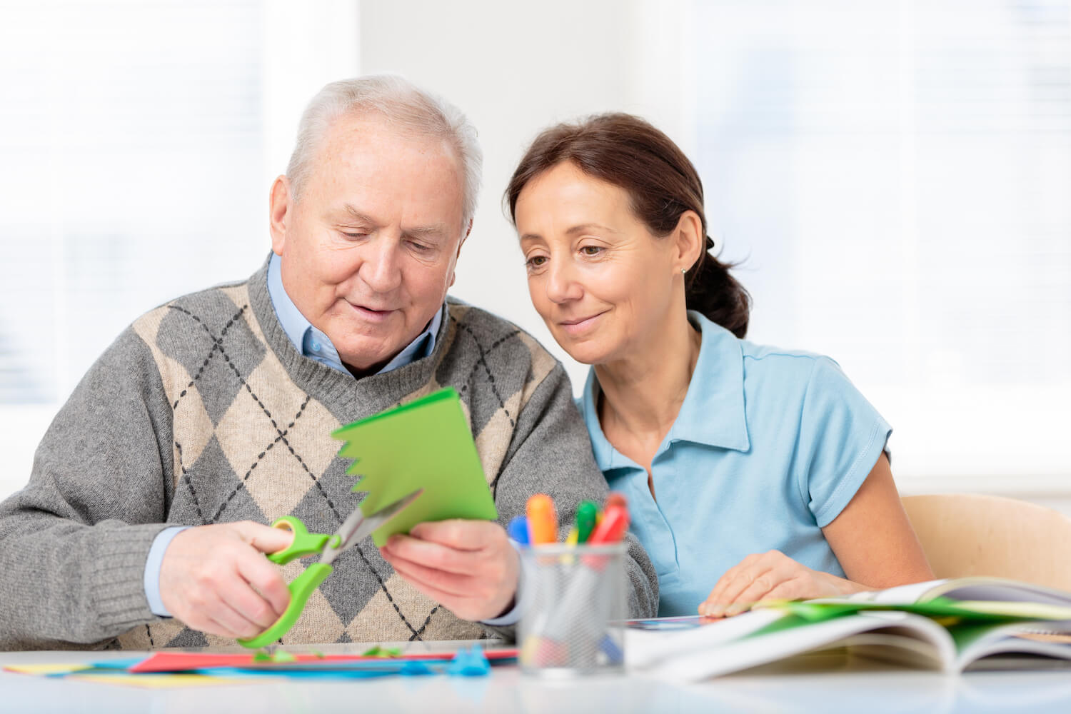 A staff member helping a senior man with a paper craft