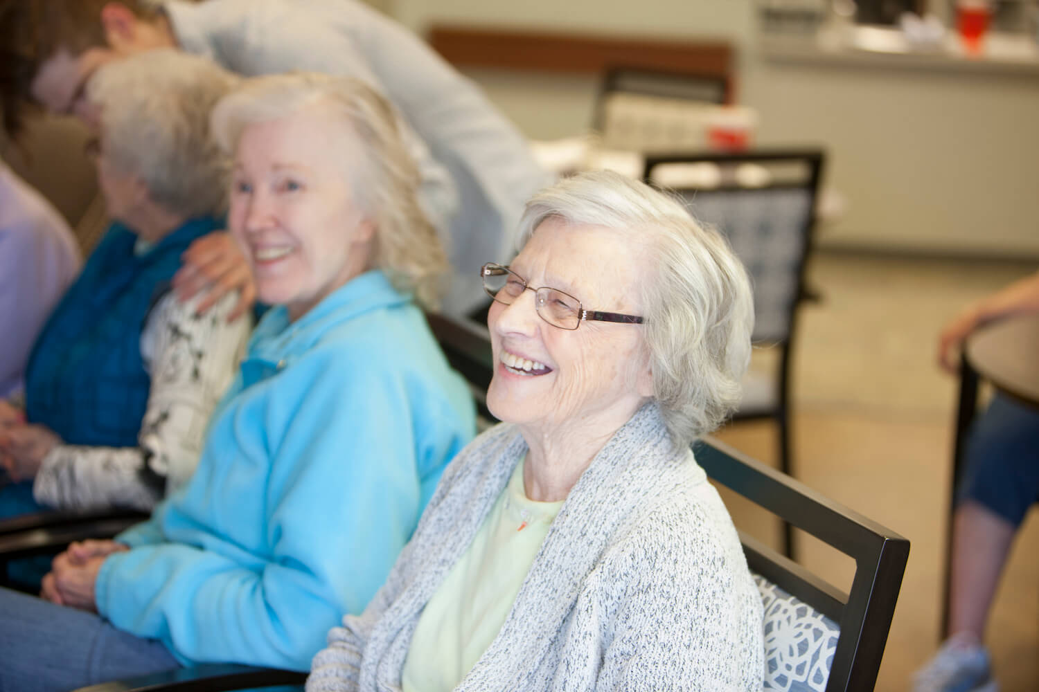 Group of senior living residents smiling and laughing together after deciding to pay for senior living care. 