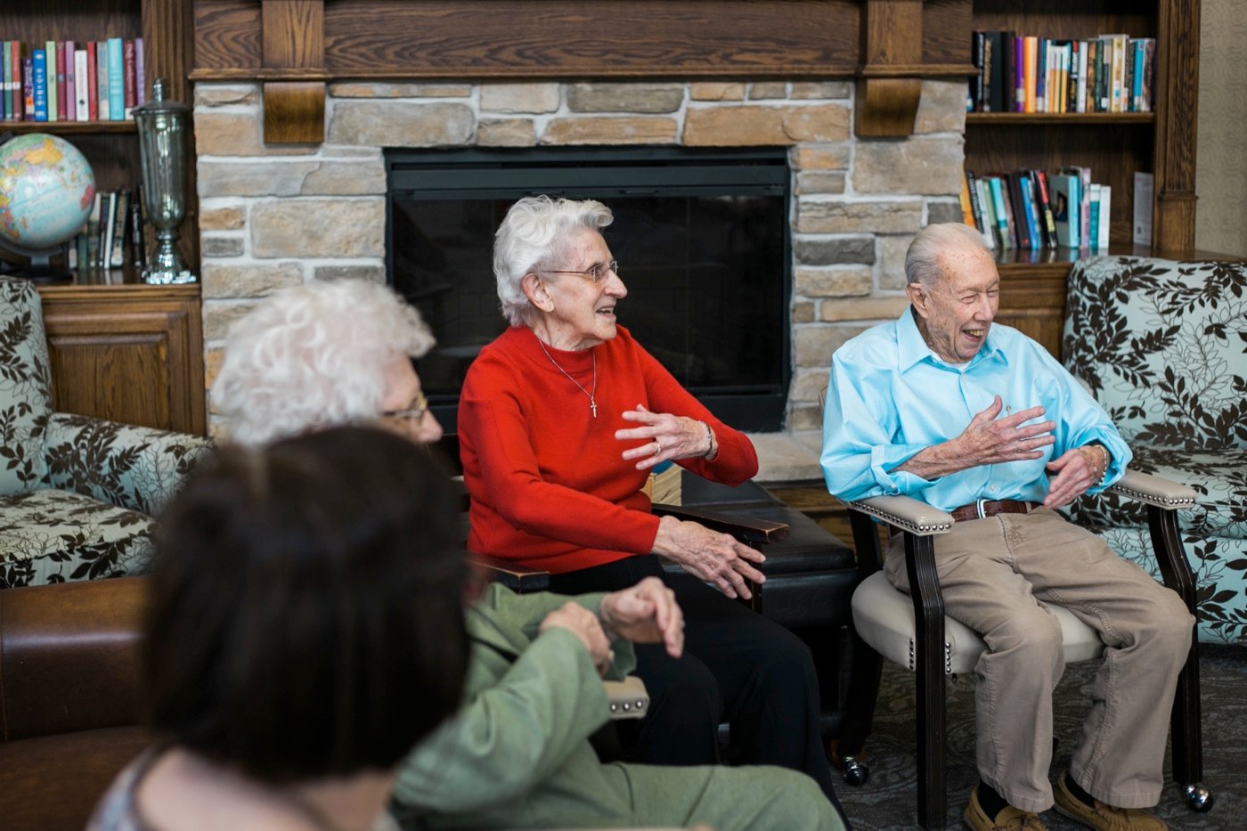 Group of seniors talking in front of the community living room fireplace