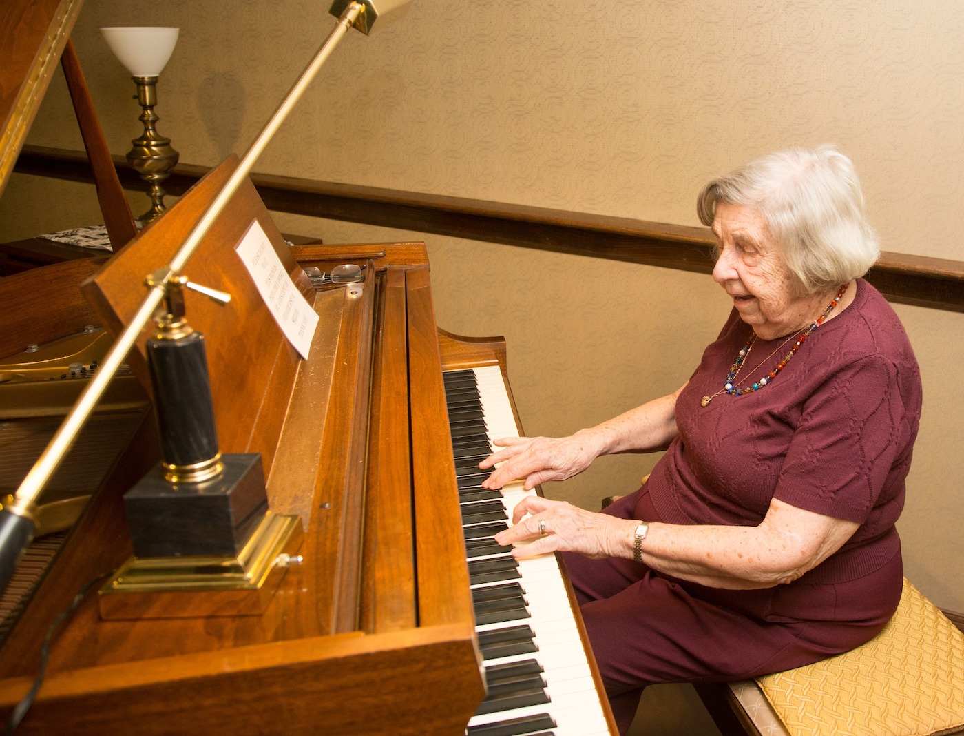 A senior woman wearing a red shirt playing a grand piano