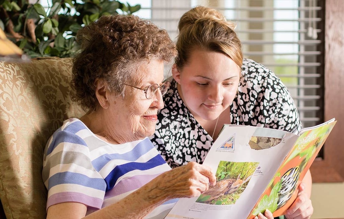 A staff member reading a magazine with a senior resident