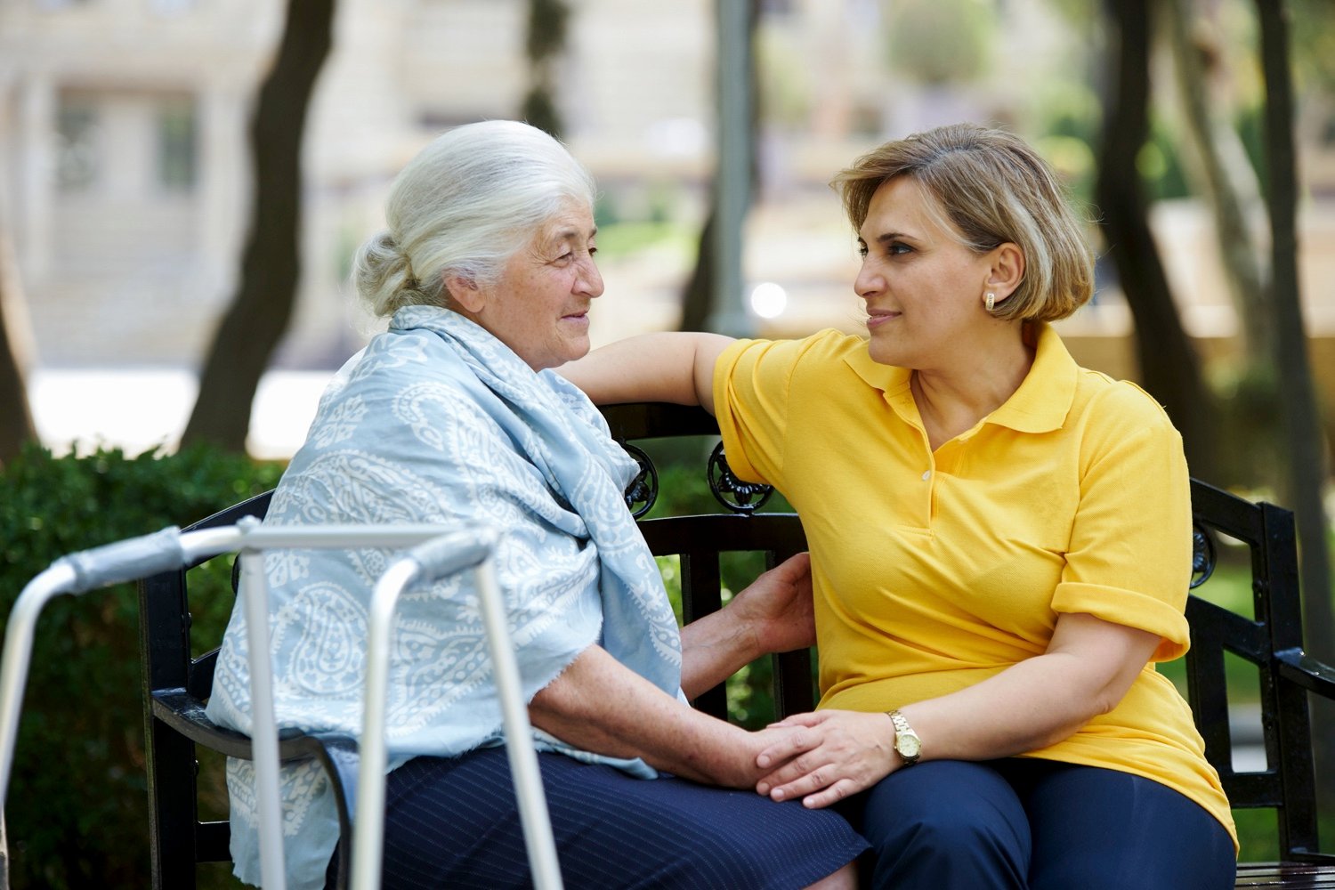 Senior woman holding hands with a caregiver on a bench in the garden