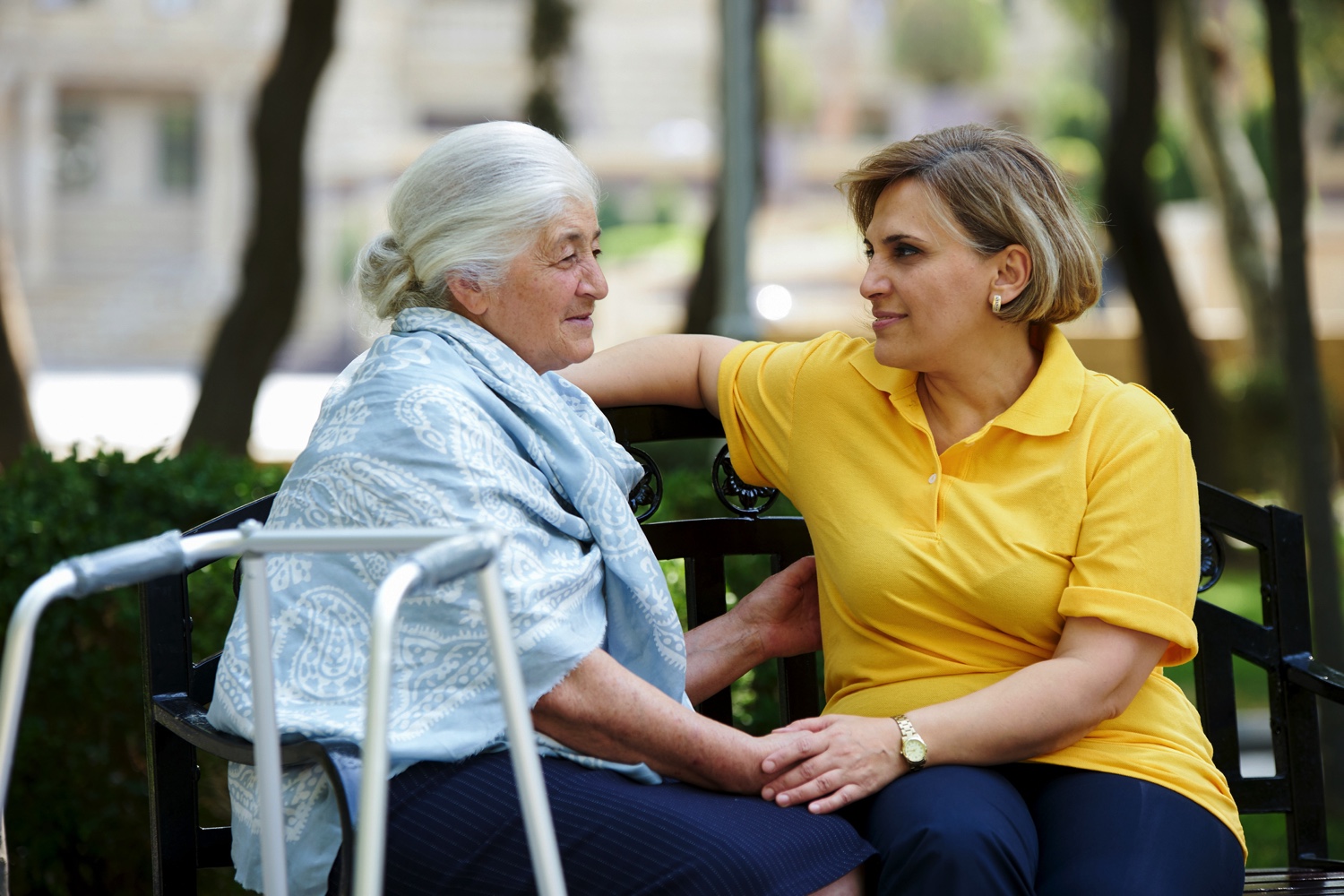 Senior woman holding hands with a caregiver on a bench in the garden