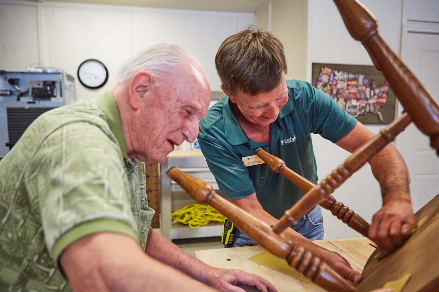 A senior and staff member work together on a woodworking project