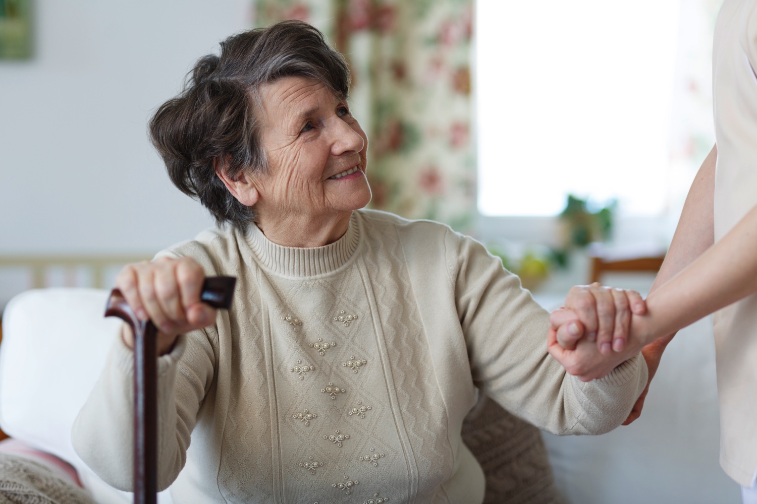 Senior woman looking up at her caregiver as they hold her hand