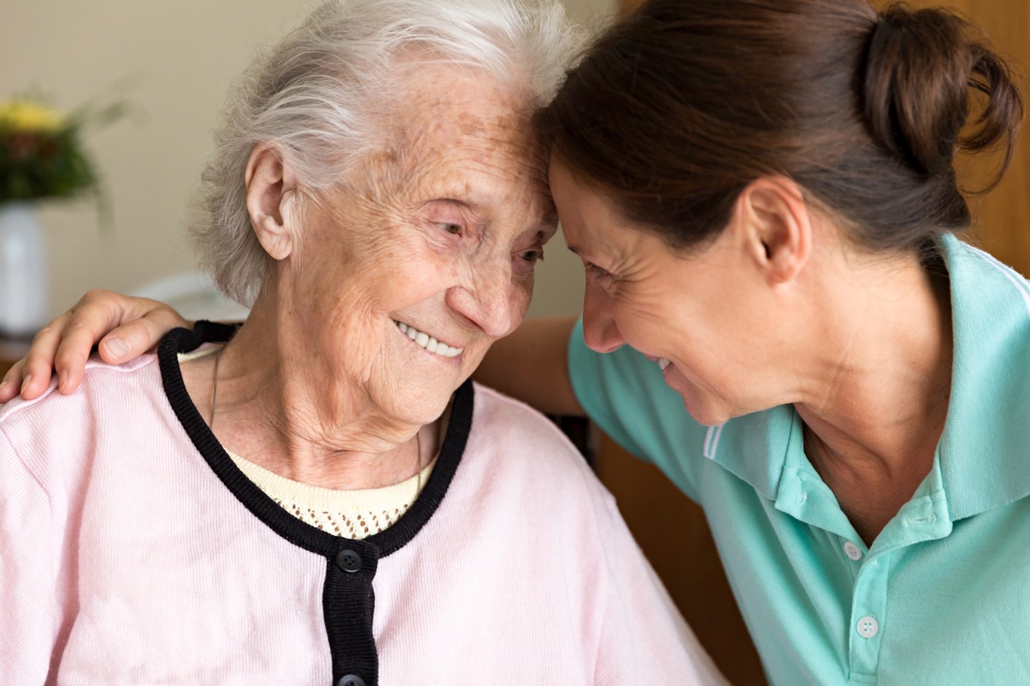 A senior woman and her carer smiling and leaning their heads together