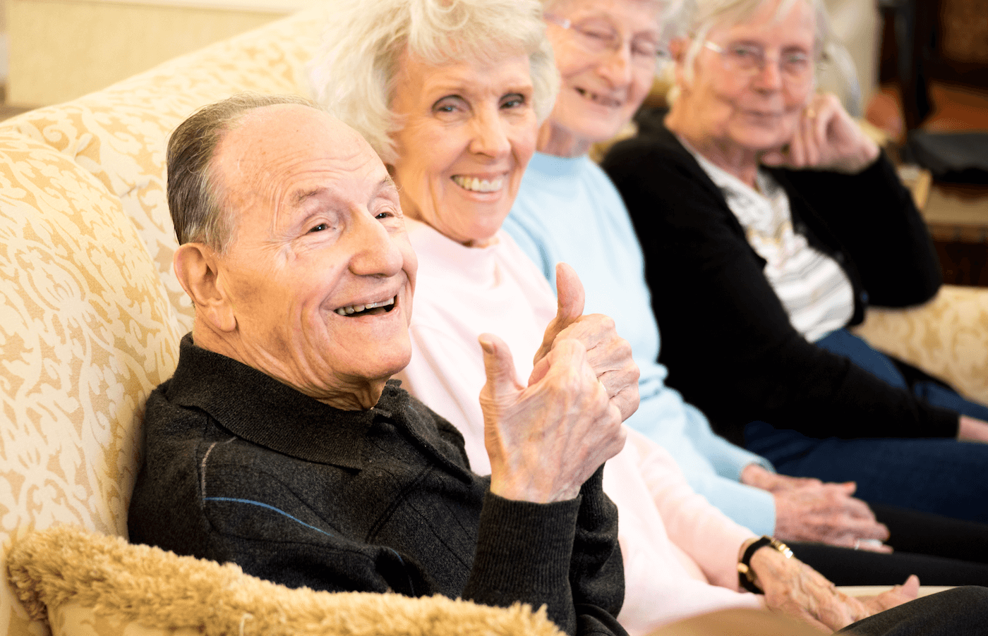 a group of four senior residents seated on a couch, and the foremost man is giving a thumbs-up