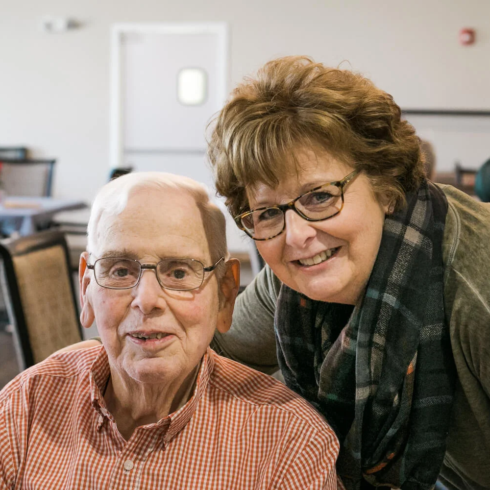 A caregiver and a resident smiling together in a dining room