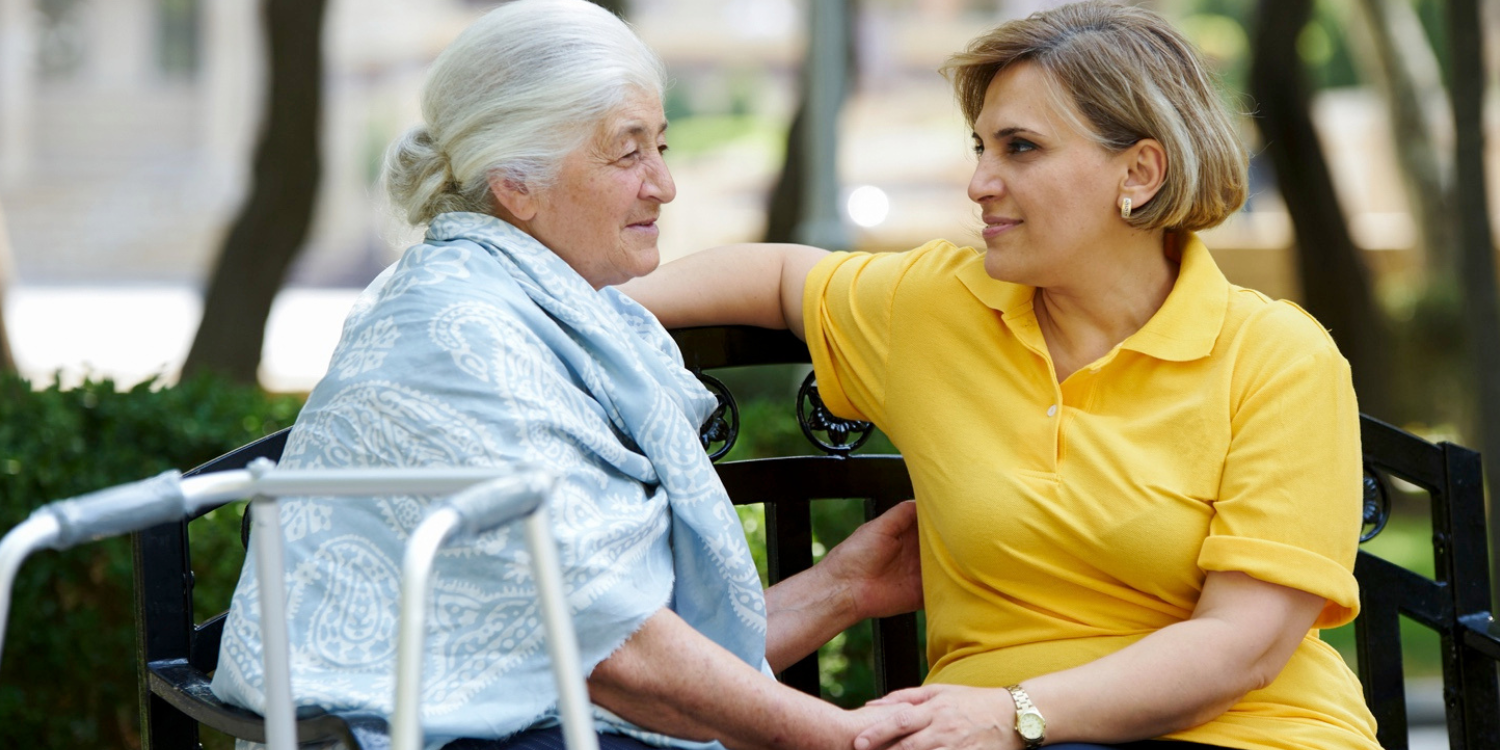 A senior woman accompanied by a woman sitting on a bench