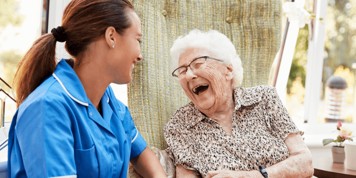 A senior living caregiver sitting and laughing with an older lady as they discuss senior living care types.