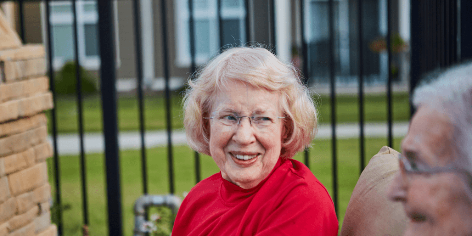 Elderly lady in red turtleneck sweater is sitting in a park listening to the reasons why senior living could benefit her.z