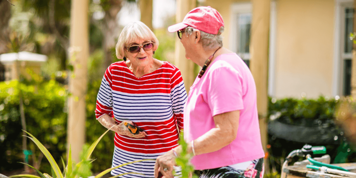 Two seniors experiencing companionship in a senior living community by chatting and gardening together outdoors