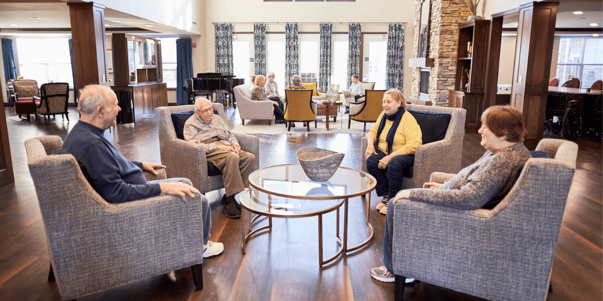 Two groups of seniors socializing in plush chairs in a senior living community lounge