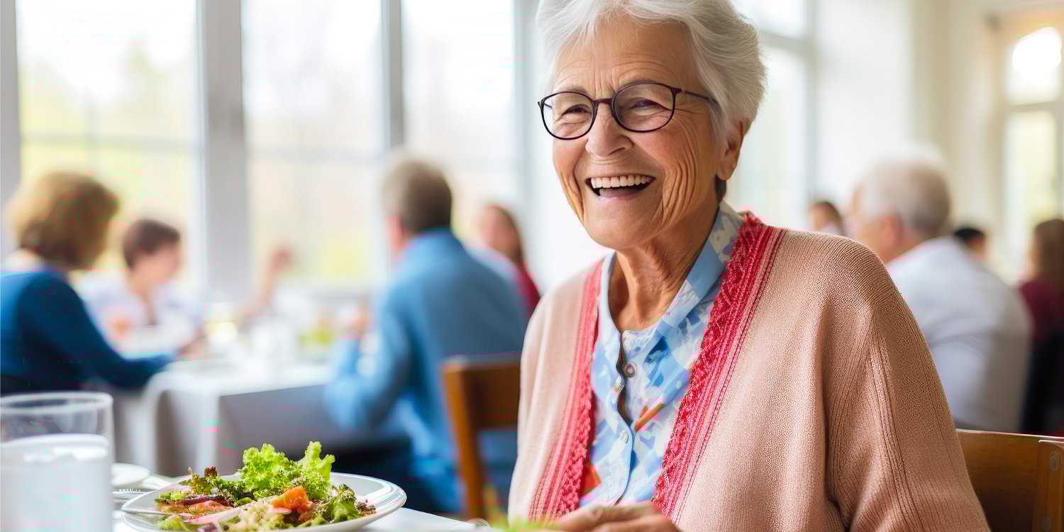 A woman in a senior living community happily enjoying a healthy lunch.
