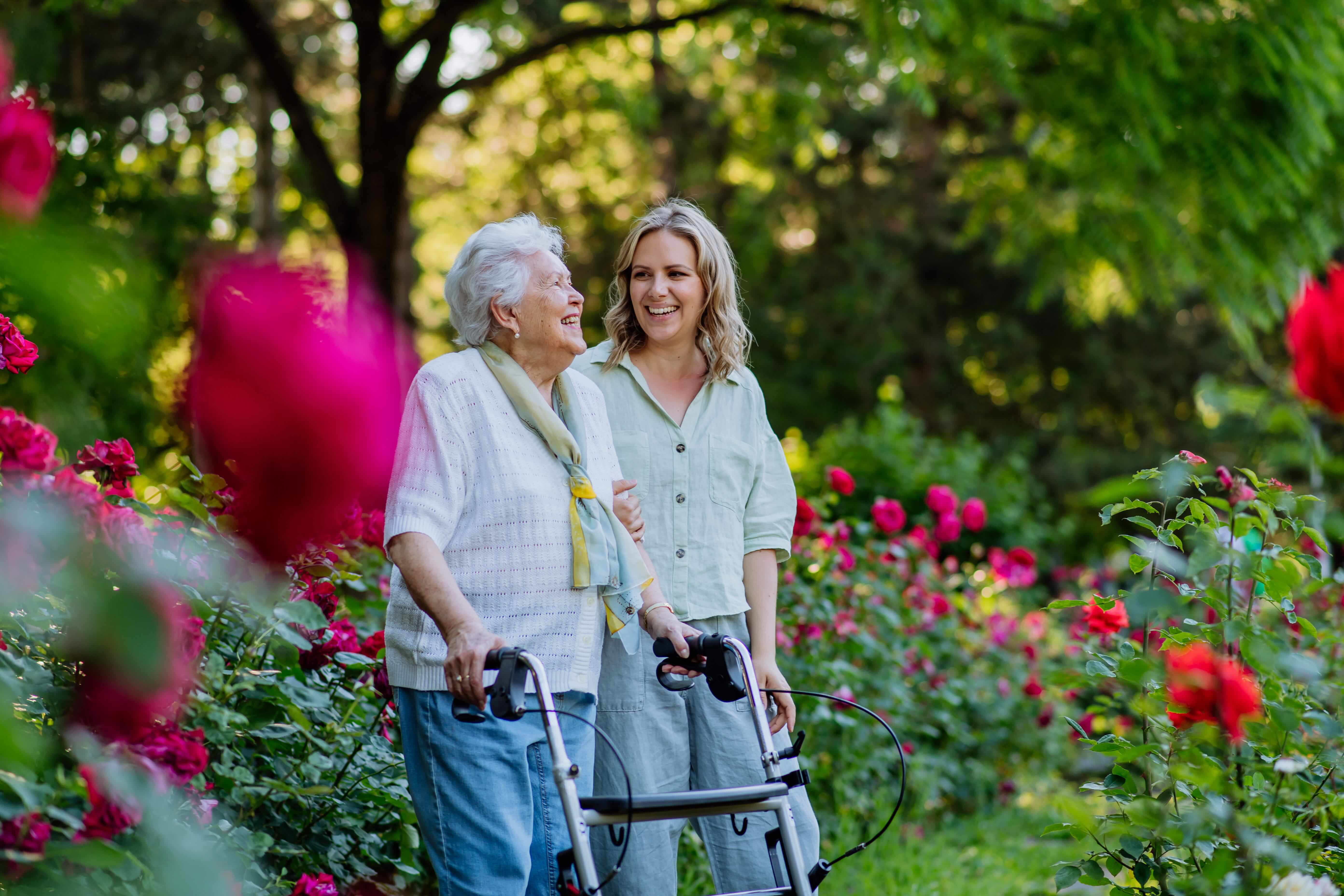 Senior living resident walking through garden with young woman.
