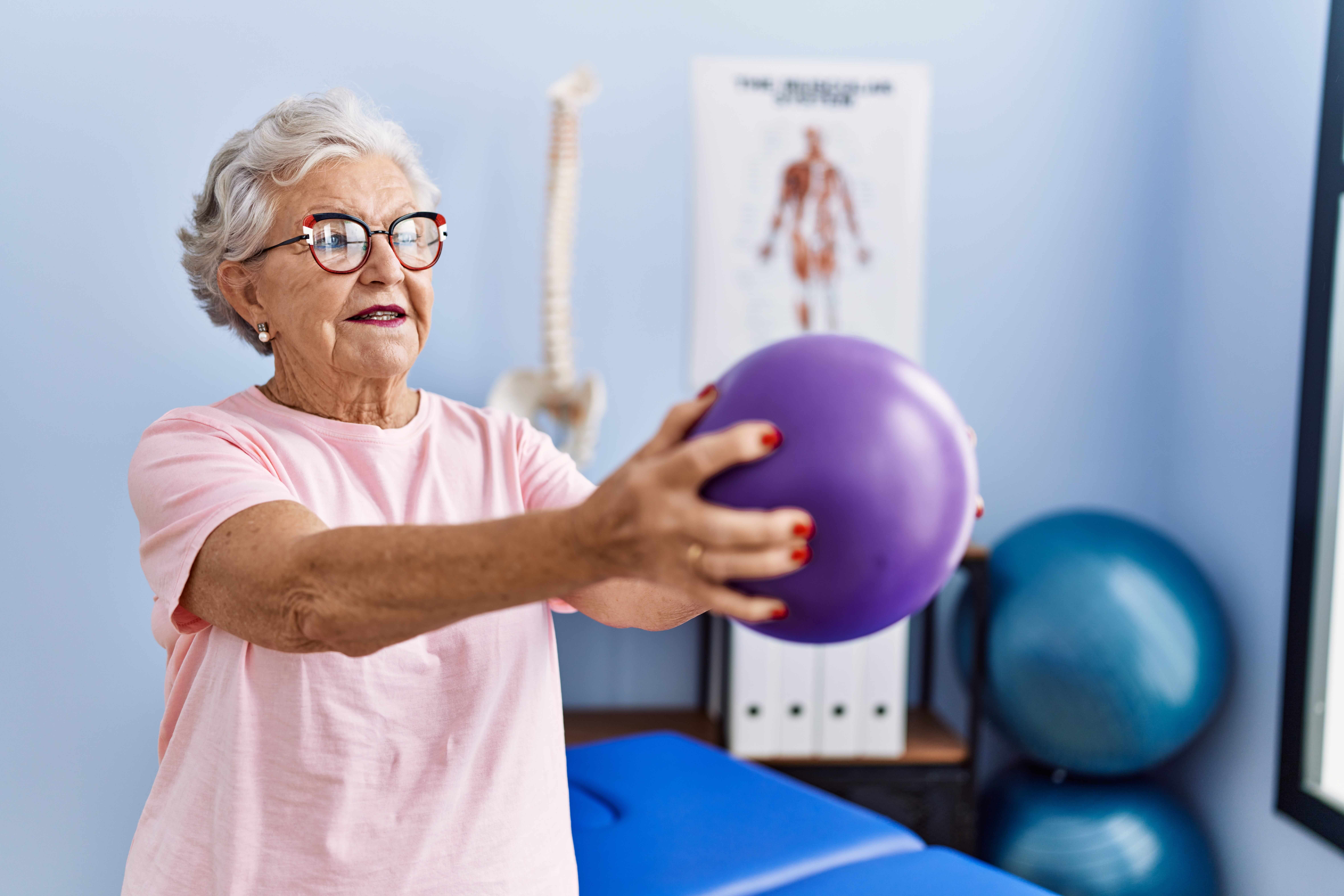 Woman in senior living lifting a purple weighted ball in physical therapy.