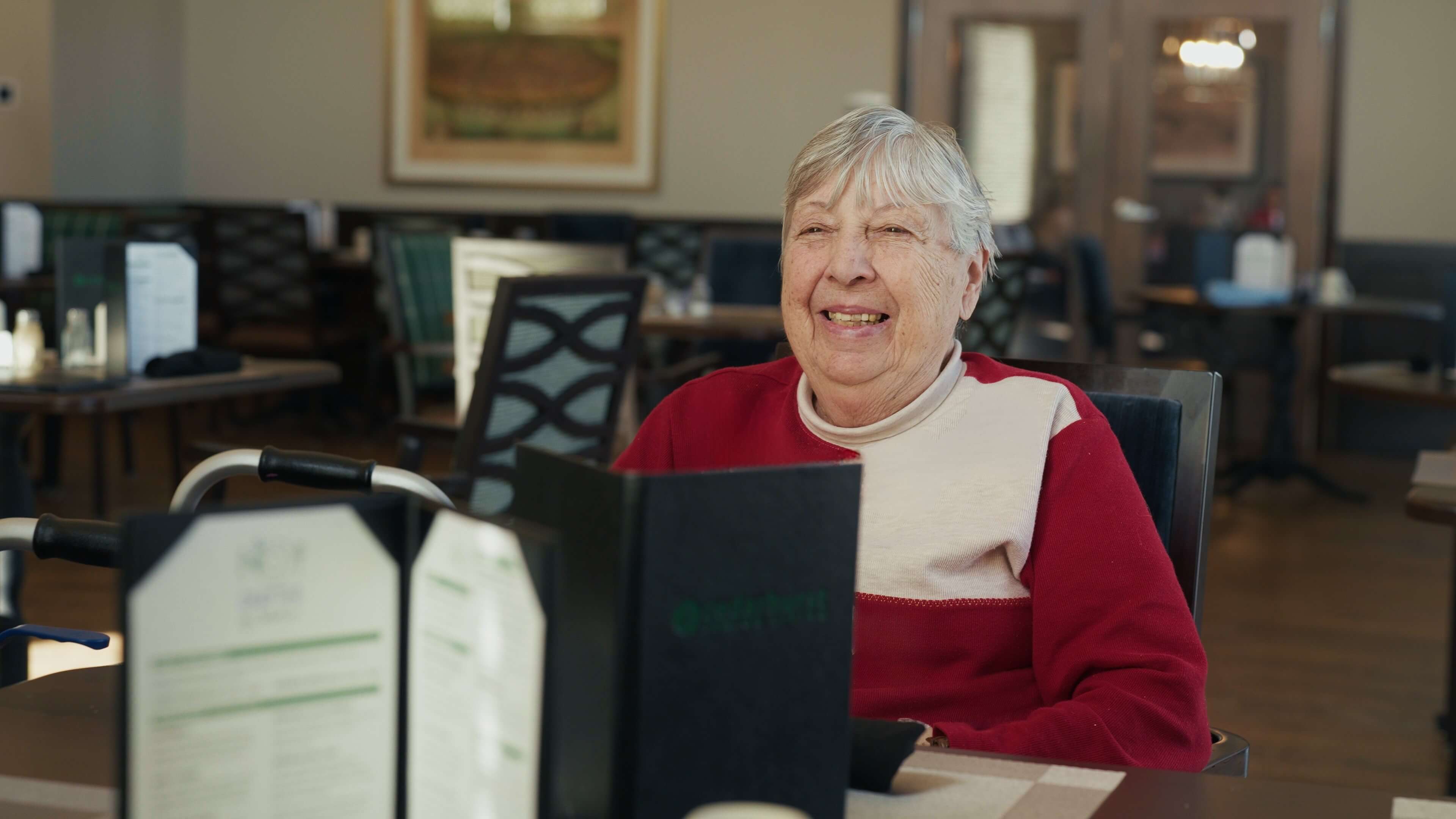 A senior woman sits in the dining room of a senior living community, looking over a menu.