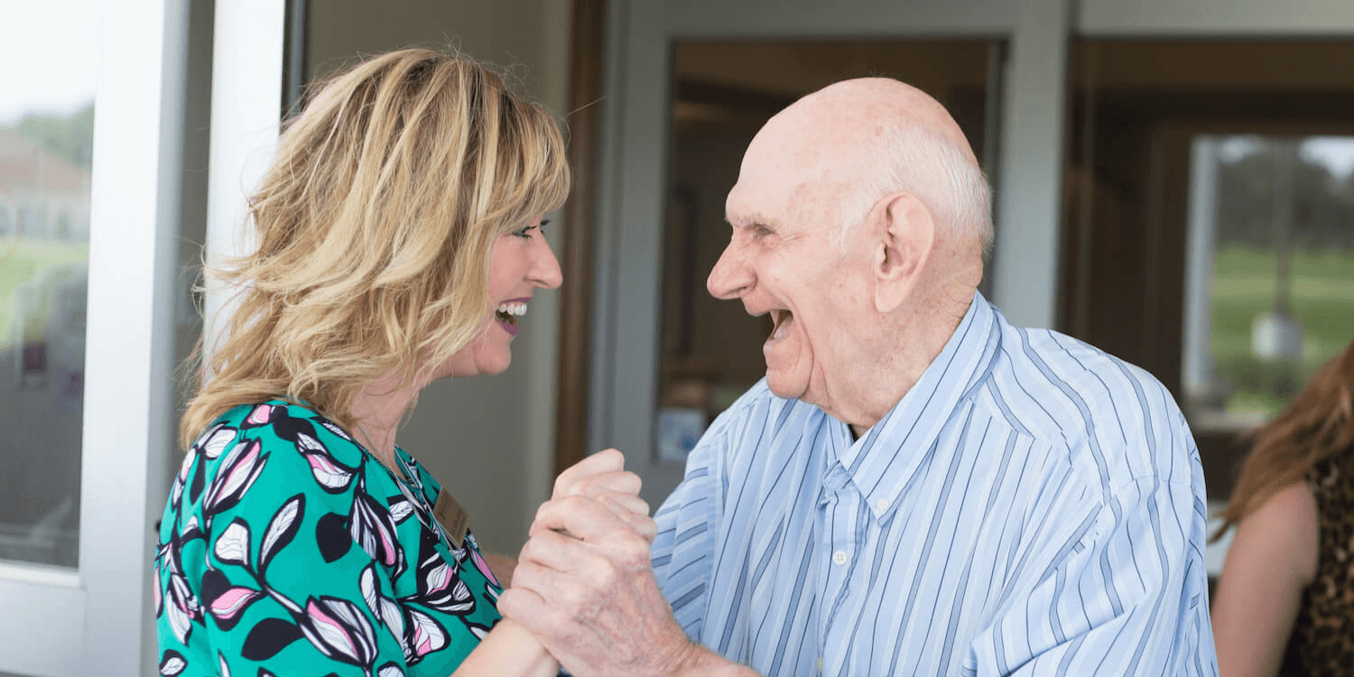 A woman with a senior living job laughing and dancing with a senior living community resident