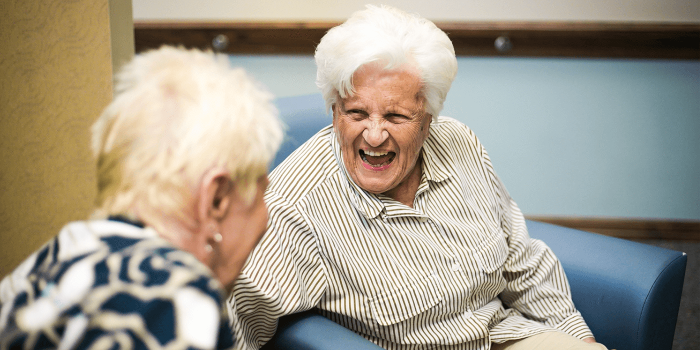 Two senior living residents sitting together and laughing