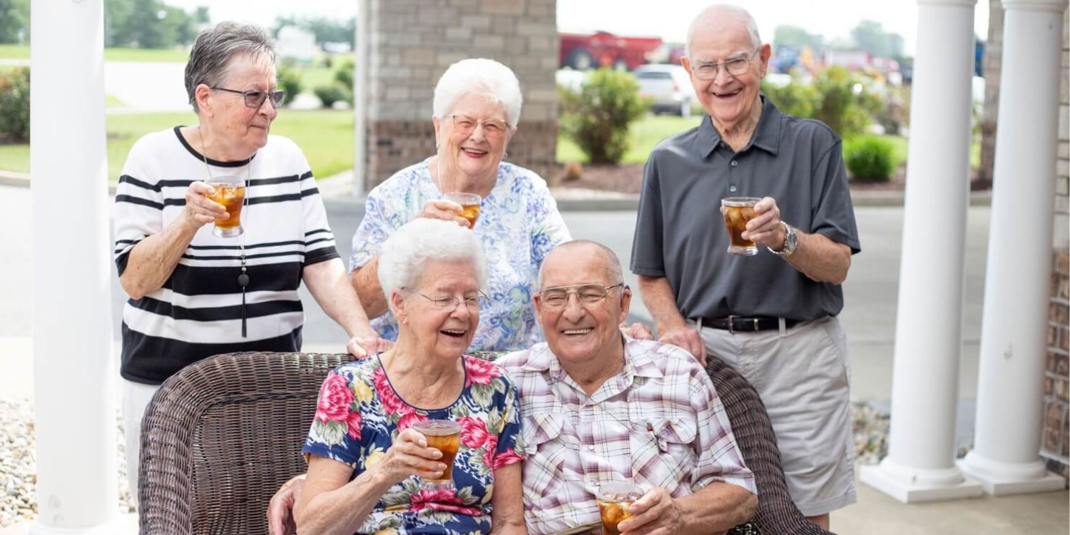 Senior residents of a community toasting drinks together while sitting outside