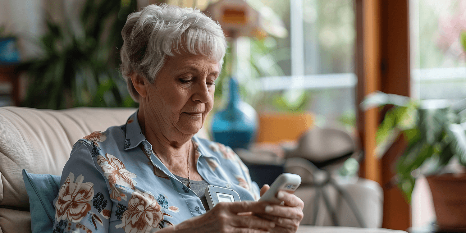  An elderly woman uses a medical alert system device to measure her health status while seated in a living room