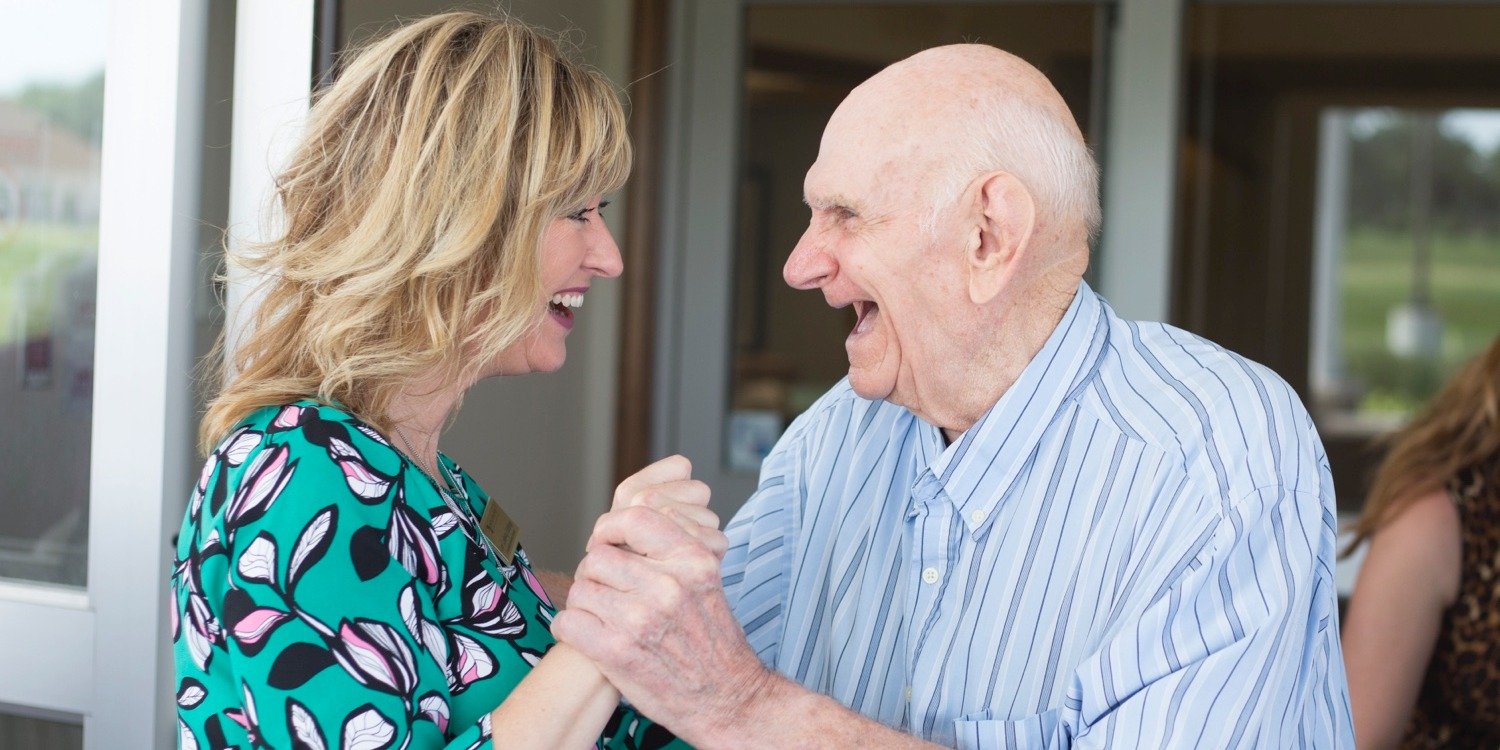 A caregiver smiling and dancing with a senior living resident