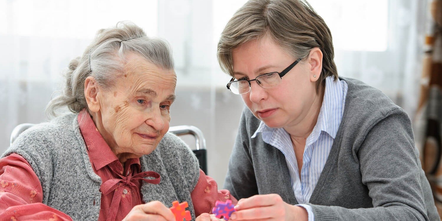 Caregiver completing a jigsaw puzzle with a senior in an assisted living community