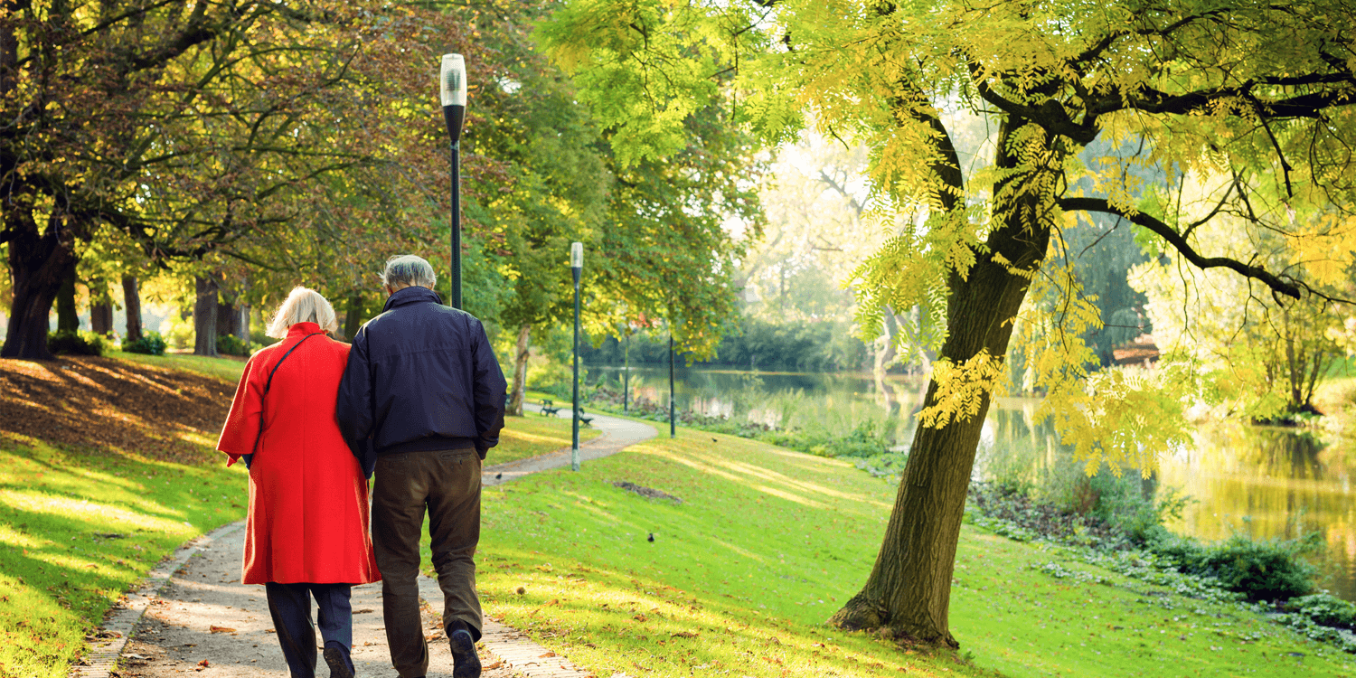 Couple on paved walking trail at senior living community surrounded by spring greenery