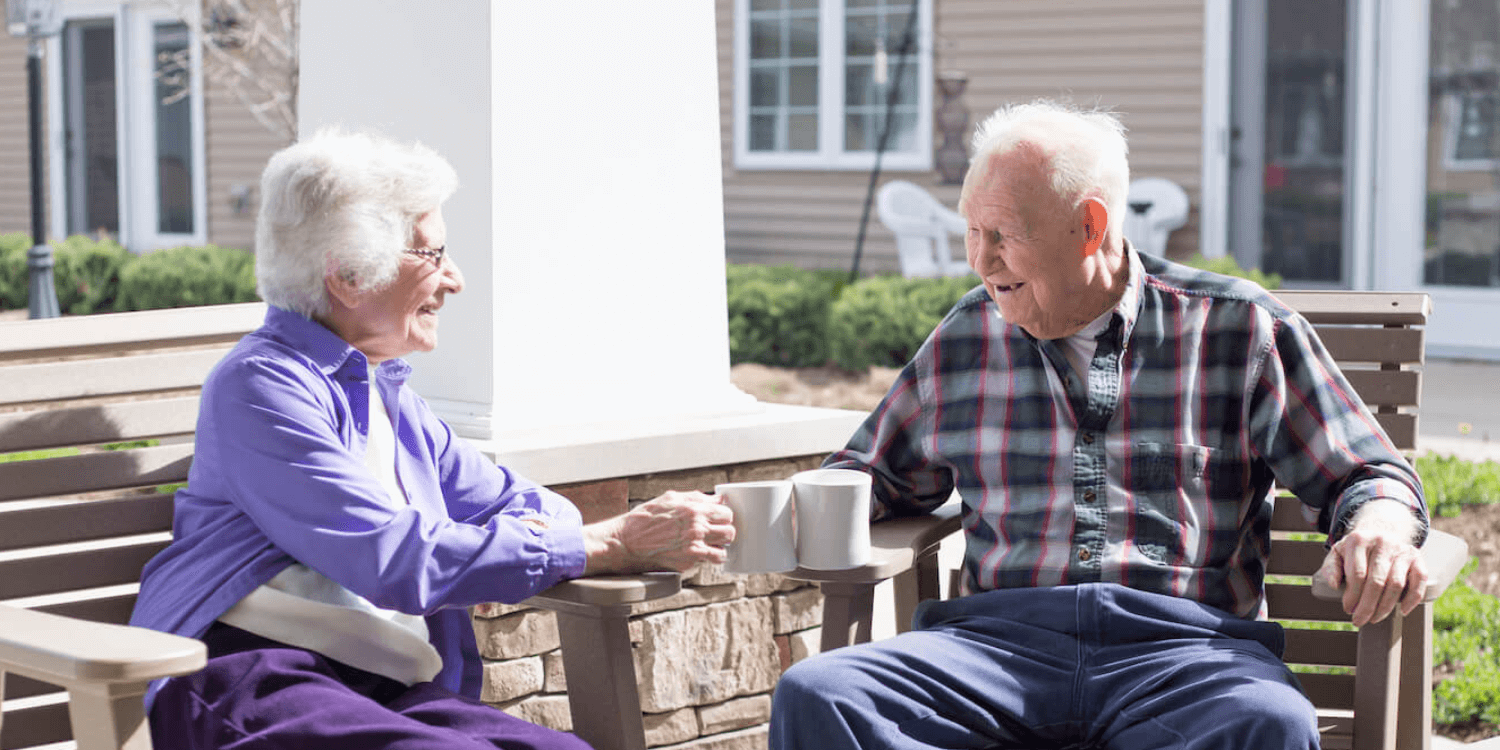 Two senior living residents enjoying coffee together while sitting outside