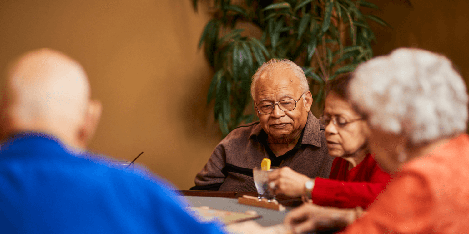 A group of seniors play a game together at a table in a memory care community.