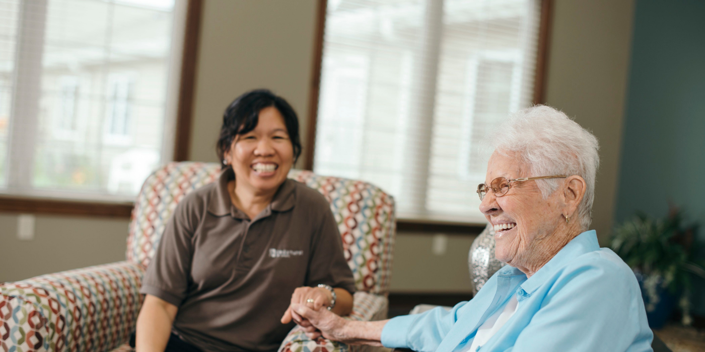 A senior living caregiver and resident are holding hands and smiling