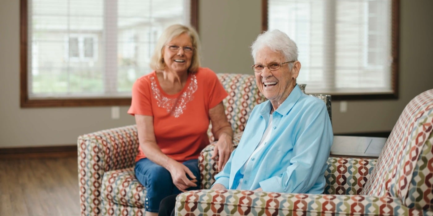 Two seniors happy about downsizing to a senior living community seated in a living room smiling at the camera