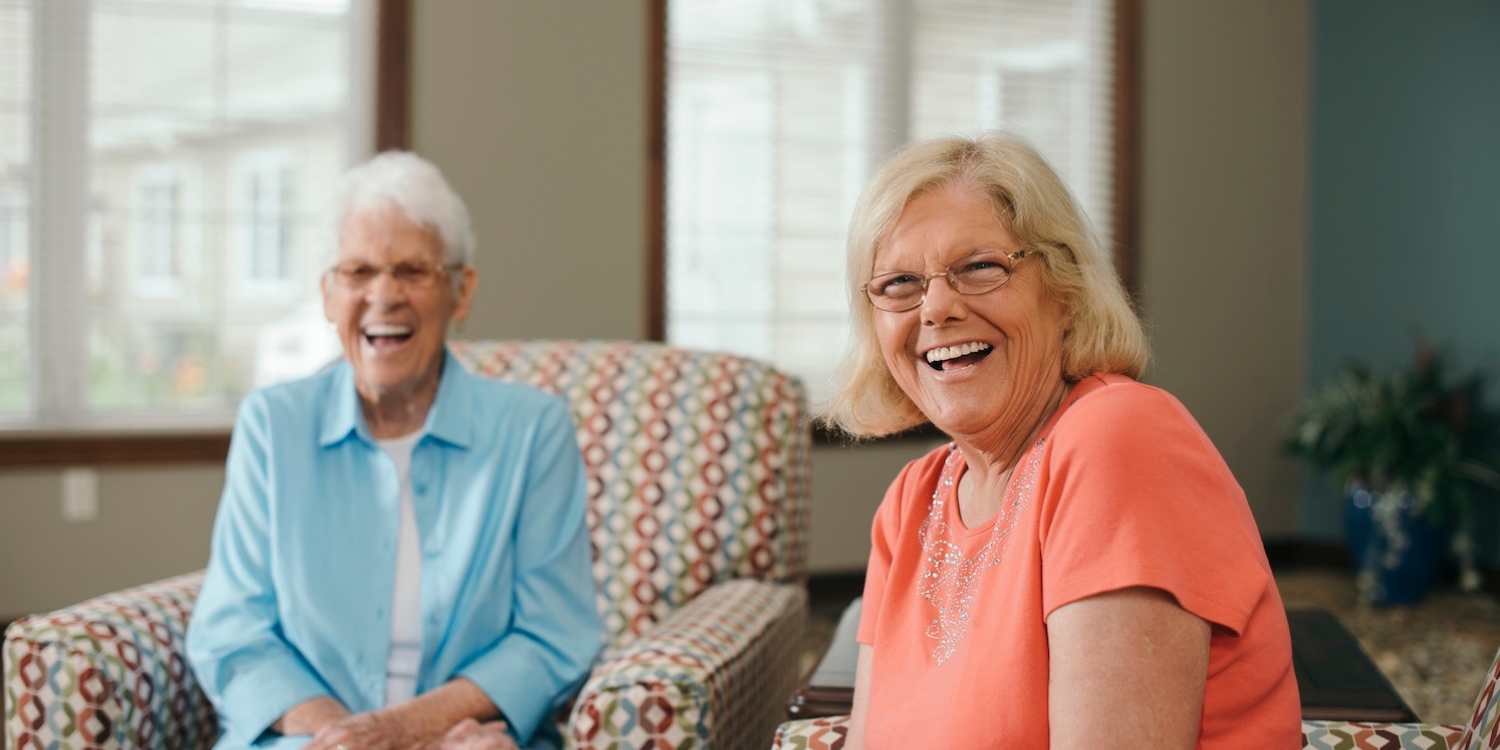 Two seniors seated in armchairs in a senior living community