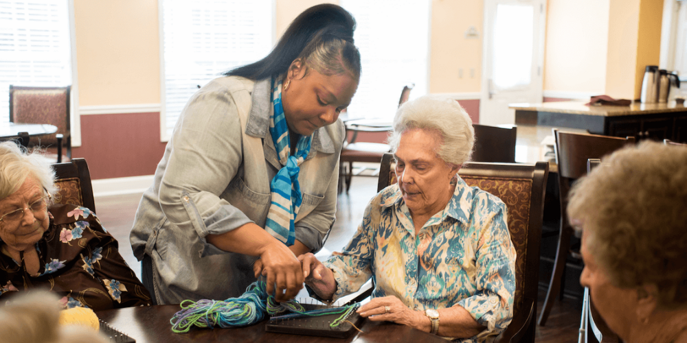 senior living community employee helping resident with activity