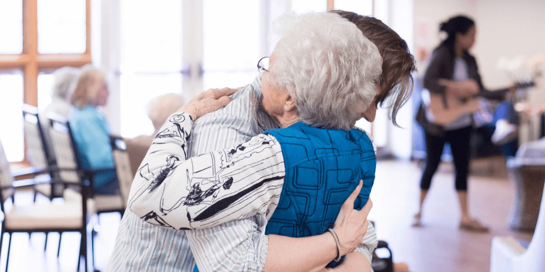 A senior living team member and resident embrace in a hug at the community.