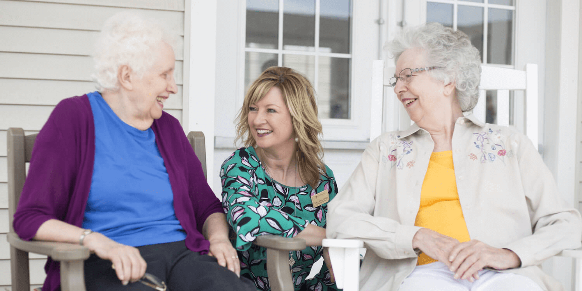 A Cedarhurst team member kneels beside two residents seated on a patio