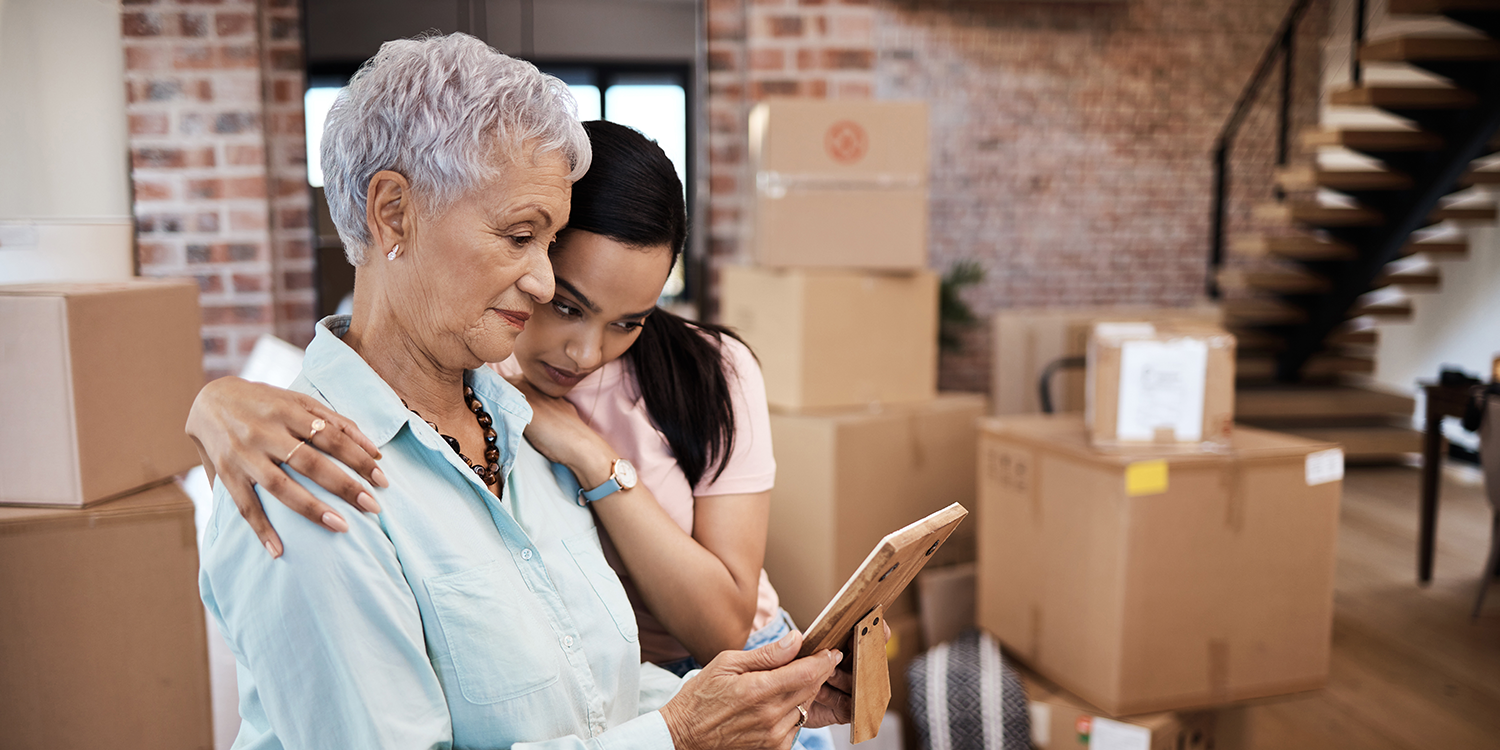 A woman and her mother look at a picture of Cedarhurst Senior Living floorplans with moving boxes in the background.