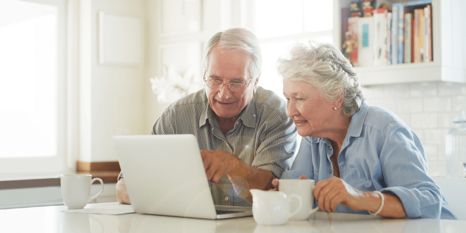 Two seniors drinking coffee and taking senior living assessments on a laptop computer at the kitchen table