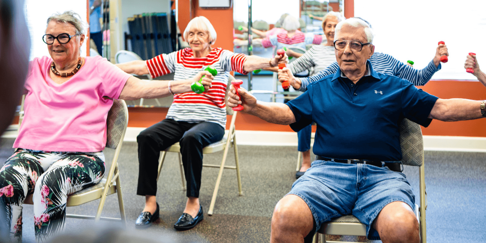 Senior residents at an active senior living community working out by lifting weights with an instructor