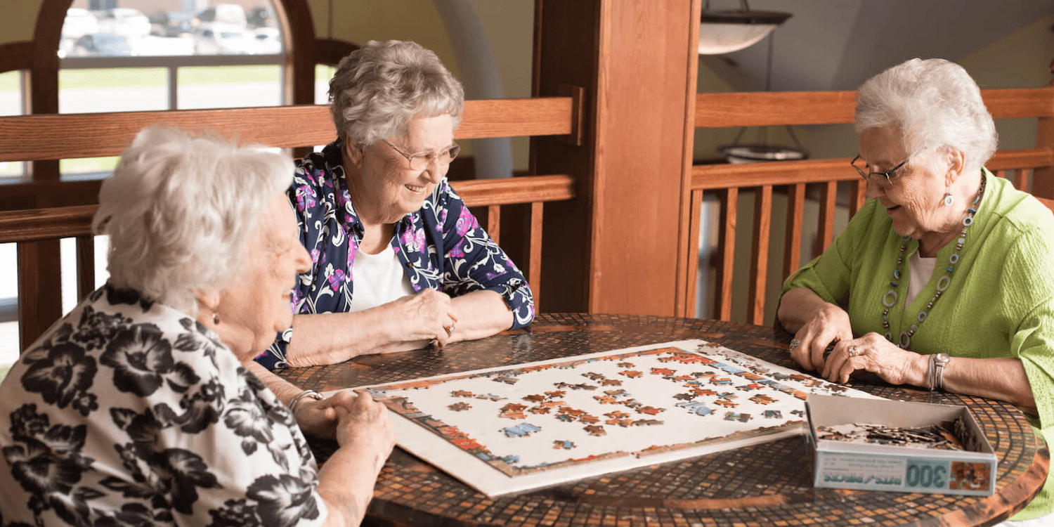 Three women engaged in a memory care activity, assembling a puzzle together as part of their cognitive exercise routine.