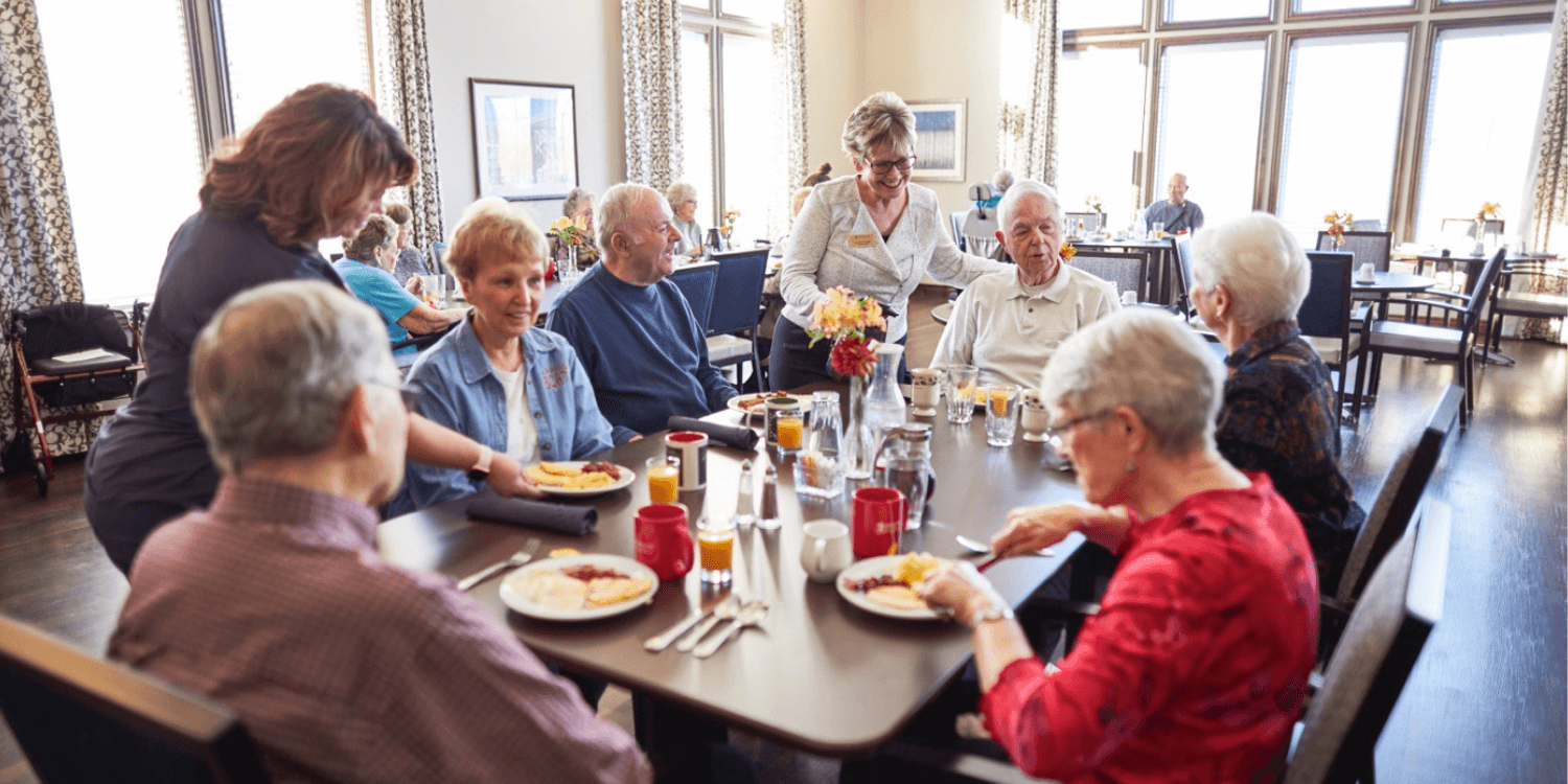 Residents eating breakfast together while being served by caregivers