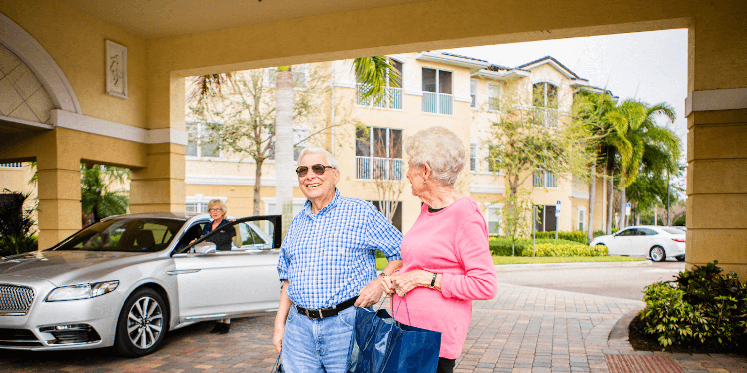 Two senior living community residents standing outside in the sun with a community driver behind them
