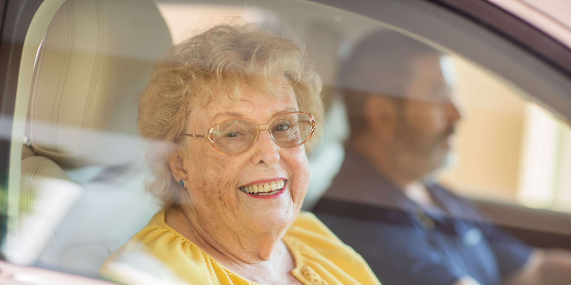 Senior resident receiving a ride from a caregiver and smiling while looking out of the window
